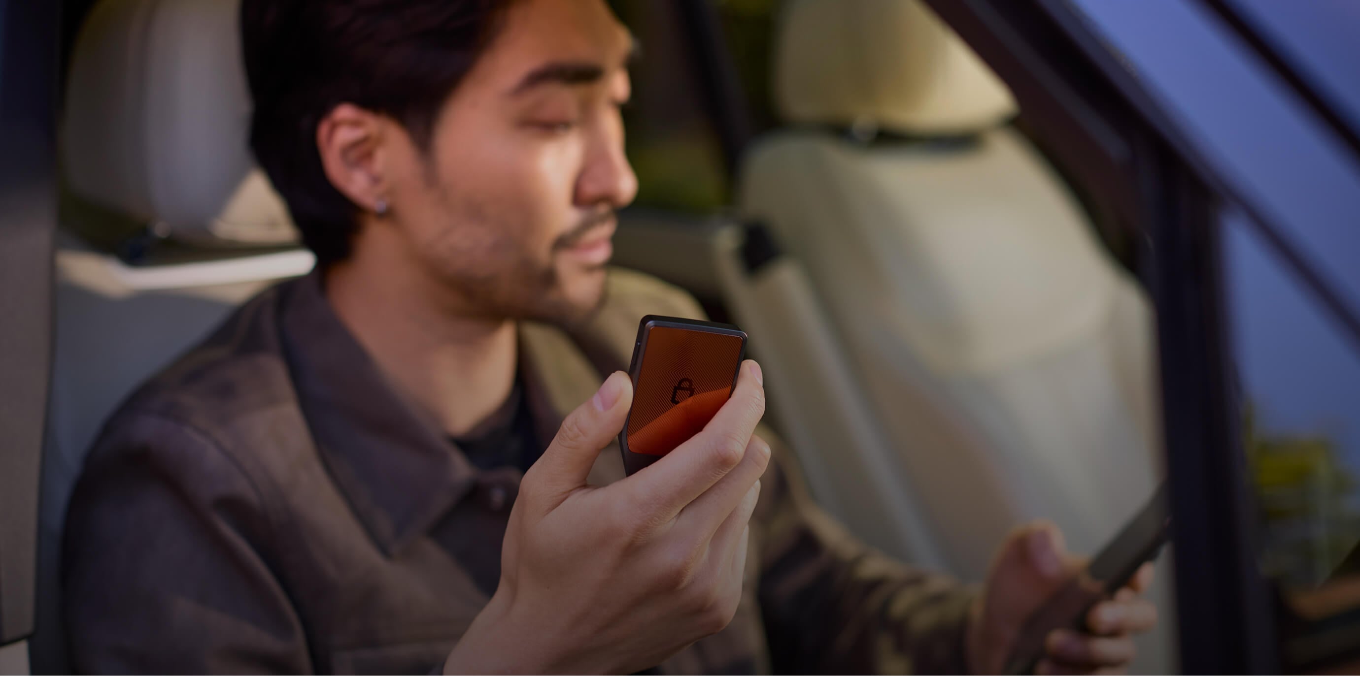 A woman sitting and looking at a Trezor Safe 7 while holding a smartphone in her other hand.