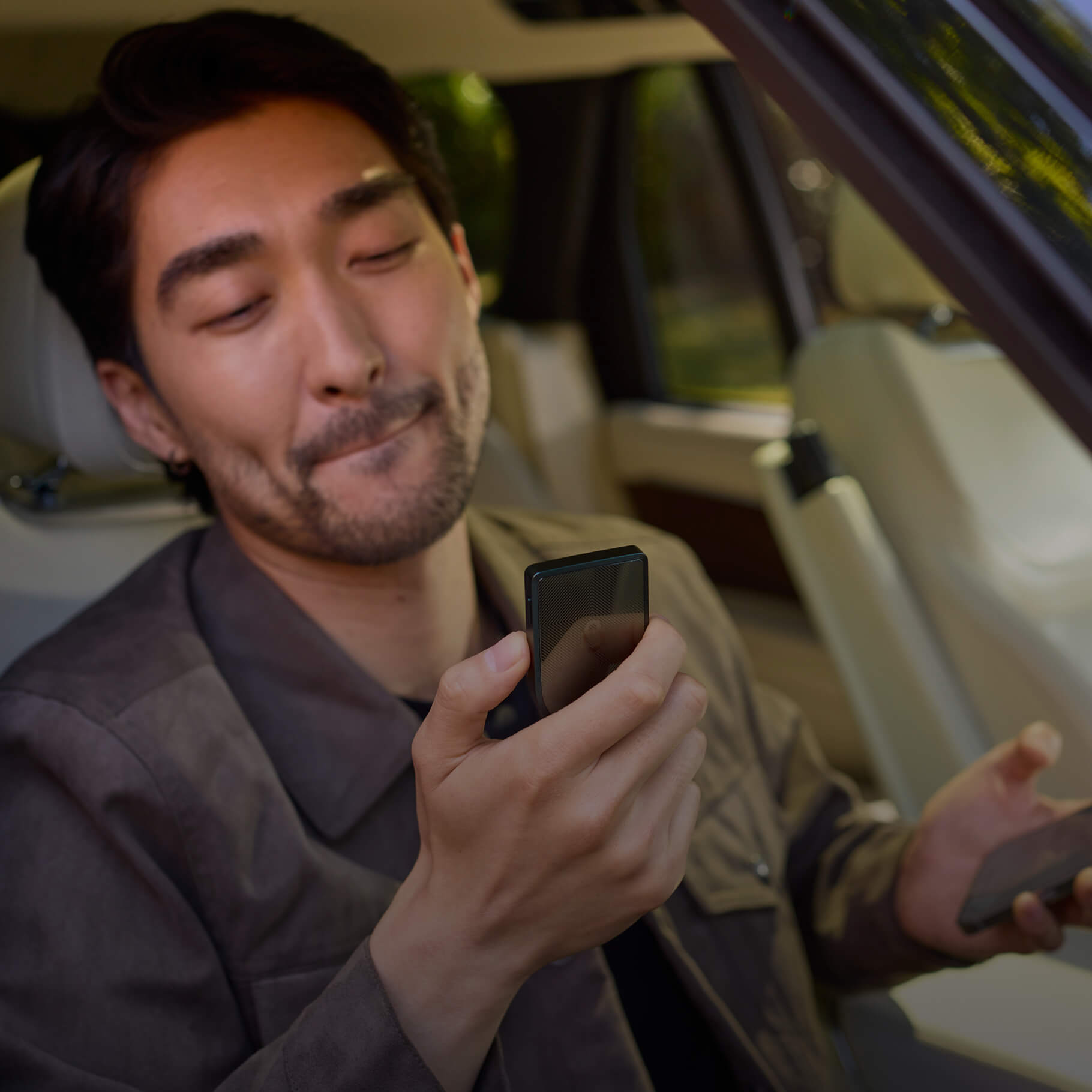 Seated man looking at a Trezor Safe 7 while holding a smartphone in his other hand.