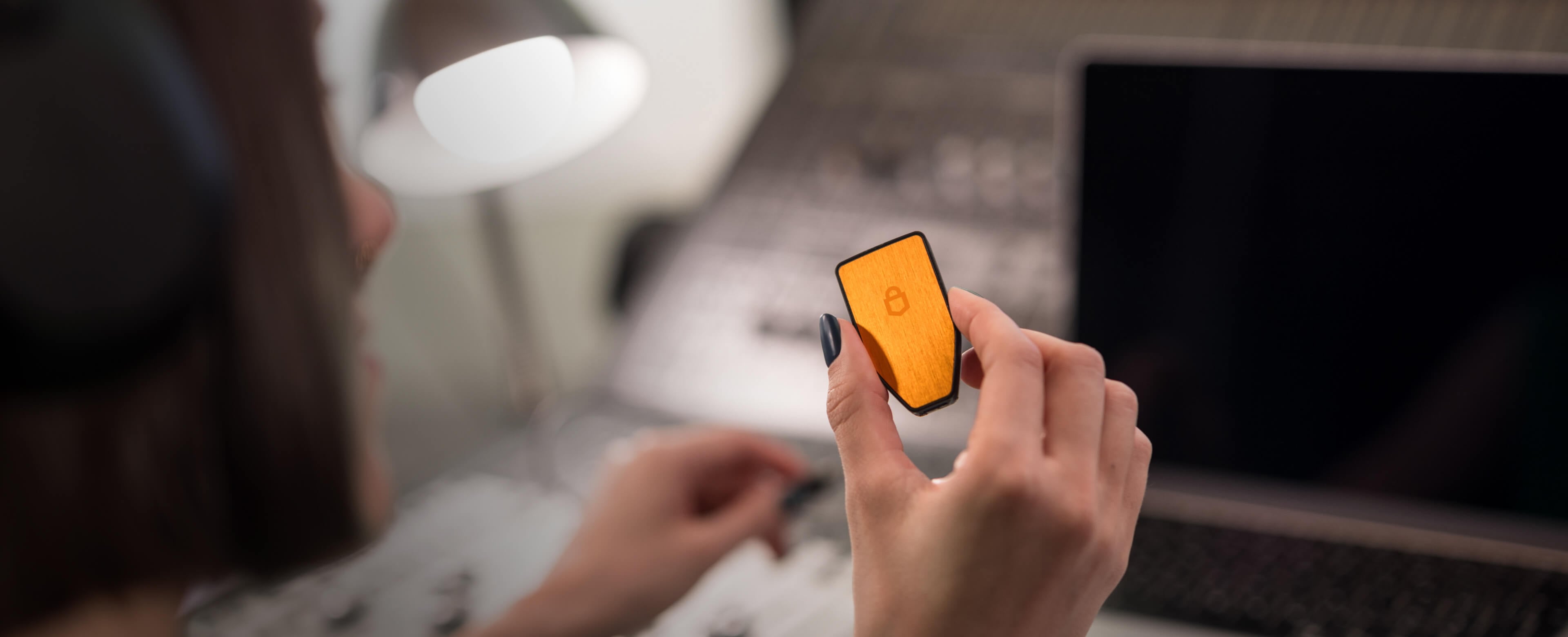Una persona con auriculares sostiene una billetera física Trezor Safe 3 en su versión solo BTC, frente a una laptop y una consola de mezcla de audio.