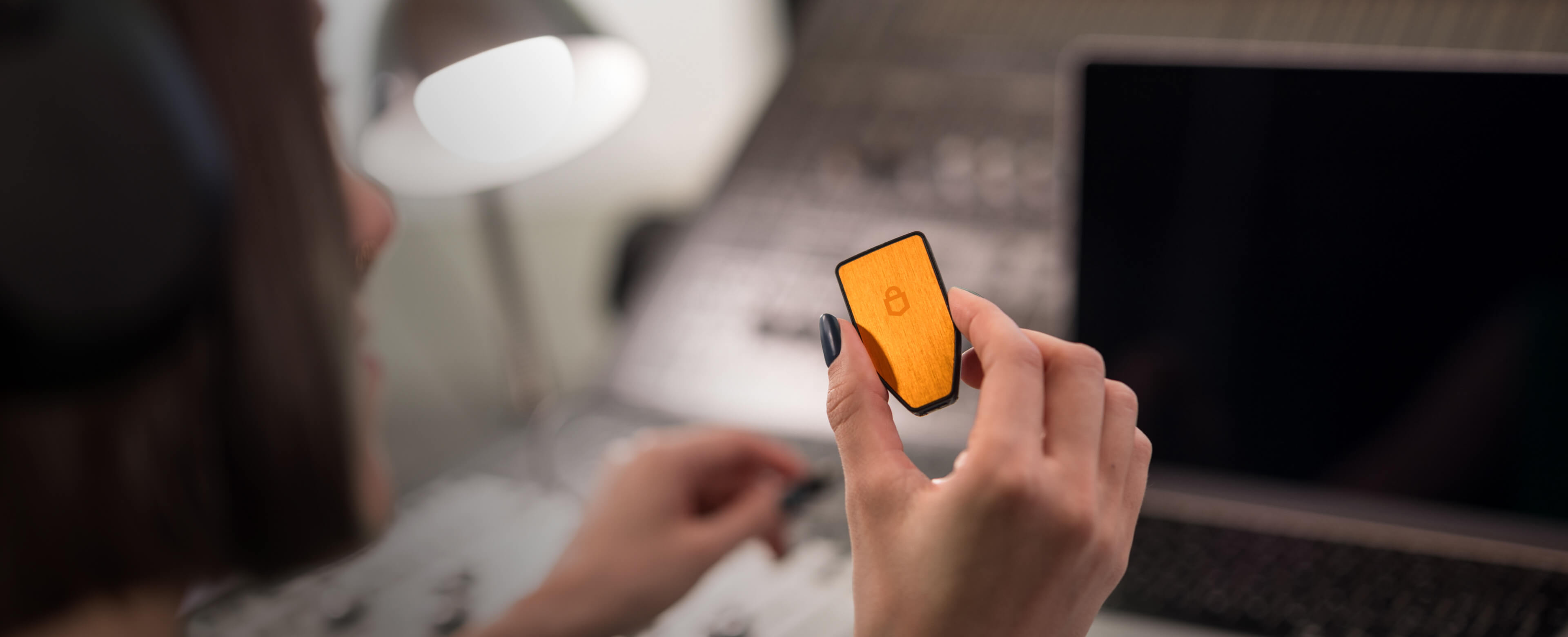 A person wearing headphones is holding a Trezor Safe 3 hardware wallet in the BTC-only version in front of a laptop and audio mixing console.