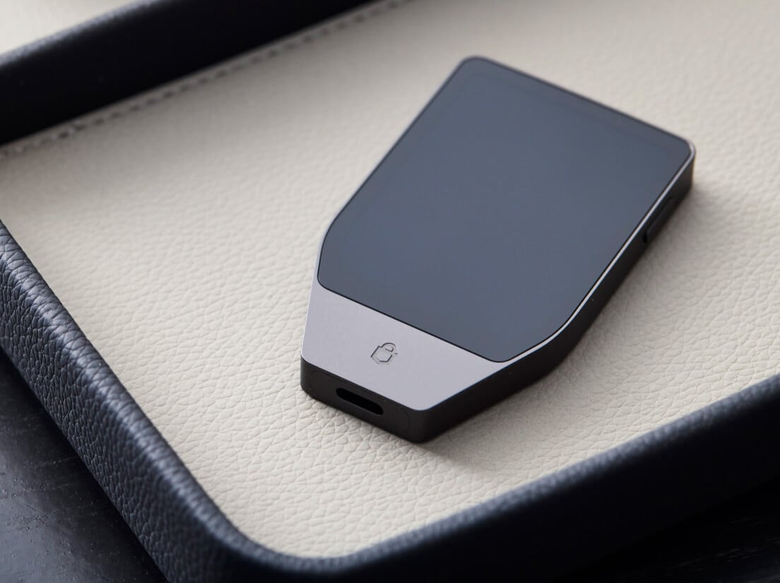 Un Trezor Safe 7 Noir Charbon posé face vers le bas sur une surface beige clair, montrant son dos et son port USB-C.