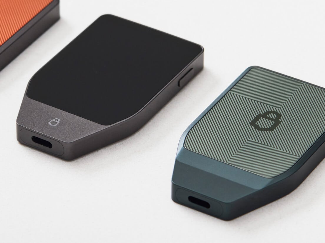 Deux appareils Trezor Safe 7, un Vert Obsidienne et un Noir Charbon, posés sur une surface blanche.