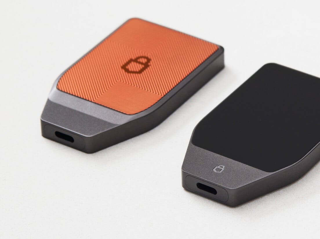 Deux appareils Trezor Safe 7, l’un en édition Bitcoin-only et l’autre en Noir Charbon, sur une surface blanche.