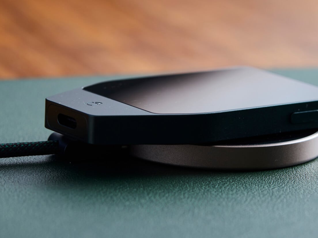 Un Trezor Safe 7 Noir Charbon posé sur un chargeur sans fil circulaire sur un bureau vert.